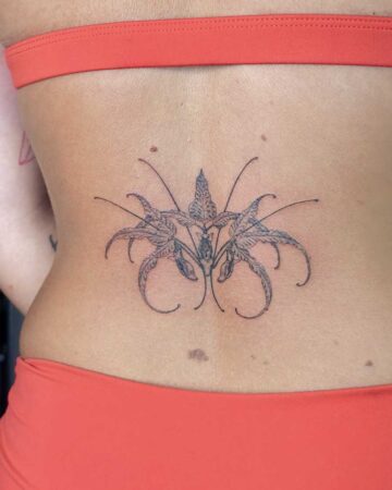 Intricate black ink floral tattoo on a lower back, featuring delicate petals and thin stems, a beautiful example of floral tattoo art. Created in the multi style tattoo studio in Canggu Bali, Bali tattoo studio, best tattoo Canggu.