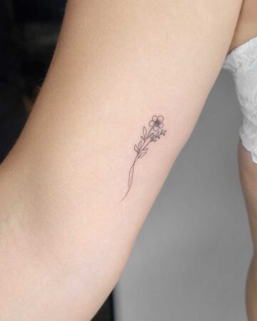 Minimalist floral tattoo of a delicate stem with a small flower and leaves on a person's arm. This fine-line tattoo is a beautiful example of floral tattoo art. Created in the multi style tattoo studio in Canggu Bali, Bali tattoo studio, best tattoo in Bali.