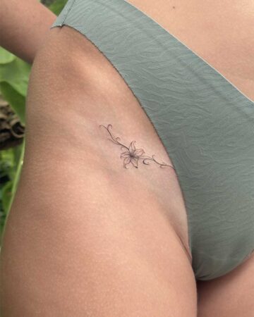 Delicate floral tattoo on the hip, featuring a minimalist lily and swirling vines. This fine-line floral tattoo is a beautiful piece of body art. Created in the multi style tattoo studio in Canggu Bali, Bali tattoo artist, best tattoo Canggu.