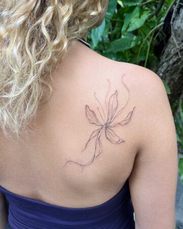 Delicate floral tattoo on a woman's shoulder, featuring thin, elegant lines of a blooming flower. This minimalist tattoo art is a beautiful example of floral tattoo designs. Created in the multi style tattoo studio in Canggu Bali, Bali tattoo studio, best tattoo in Bali, tattoo artist Canggu.