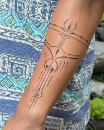 Close-up of an ornamental tattoo on an arm, featuring intricate geometric lines and abstract shapes resembling a stylized sword and celestial elements. This ornamental tattoo showcases fine-line artistry. Created in the multi style tattoo studio in Canggu Bali, Bali tattoo artist.