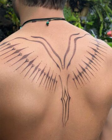 Close-up of a man's back featuring an intricate ornamental tattoo of stylized wings extending from the spine, rendered in fine black linework and dotwork. This ornamental tattoo showcases a unique artistic design. Created in the multi style tattoo studio in Canggu Bali, Bali tattoo studio, tattoo Canggu.