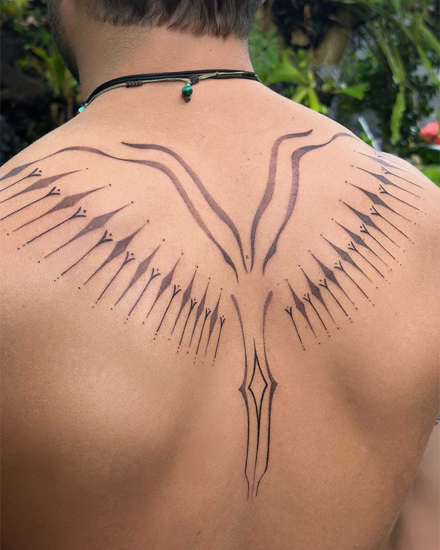Close-up of a man's back featuring an intricate ornamental tattoo of stylized wings extending from the spine, rendered in fine black linework and dotwork. This ornamental tattoo showcases a unique artistic design. Created in the multi style tattoo studio in Canggu Bali, Bali tattoo studio, tattoo Canggu.